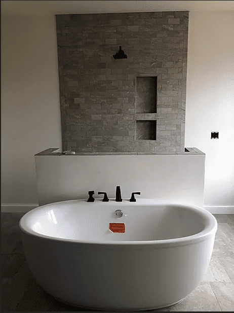 A bathroom with a large white tub and tiled walls.
