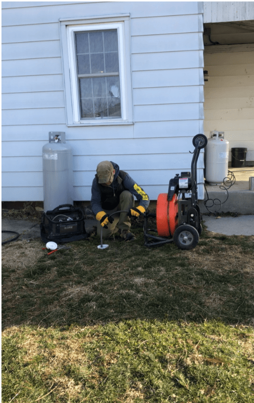 A man kneeling down next to a pipe.